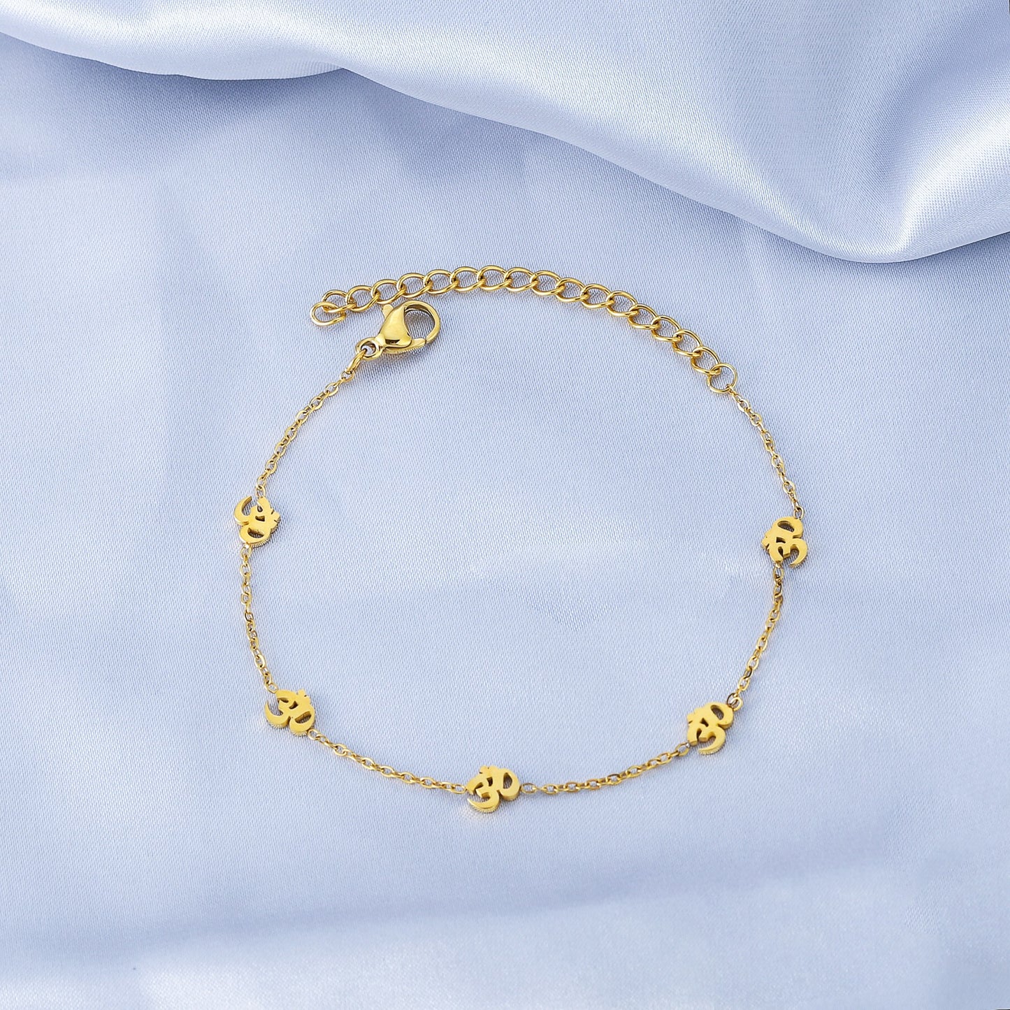 Gold bracelet with small round charms on a light blue satin background