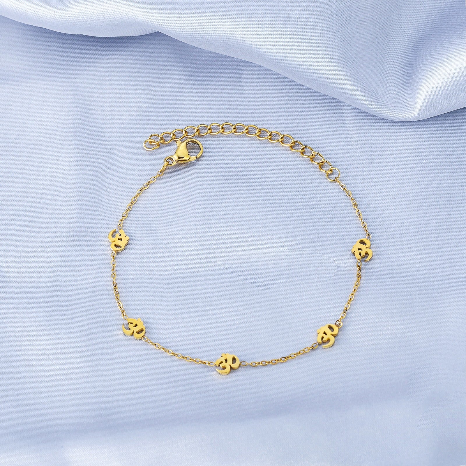 Gold bracelet with small round charms on a light blue satin background