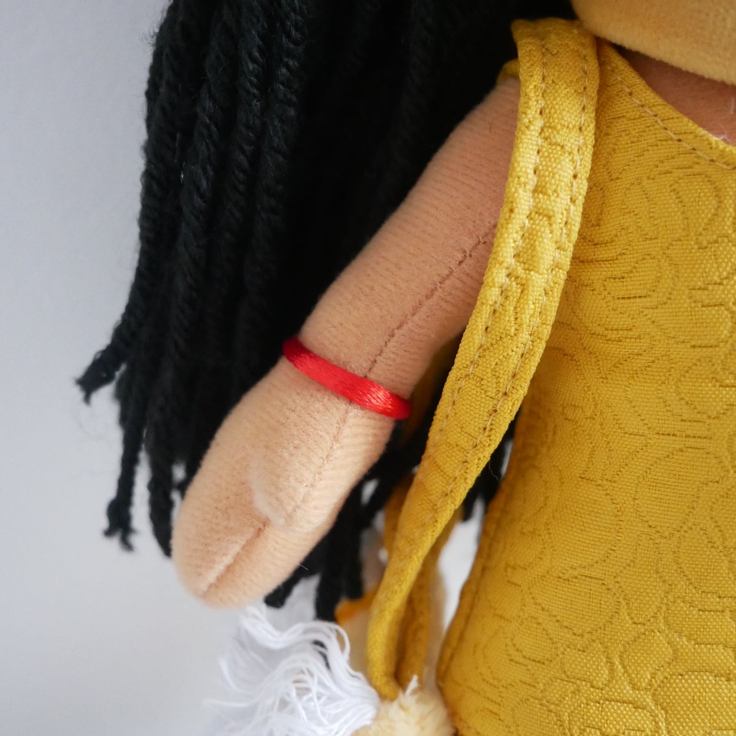 Doll with yellow outfit, black braids, and red bandage on a white background