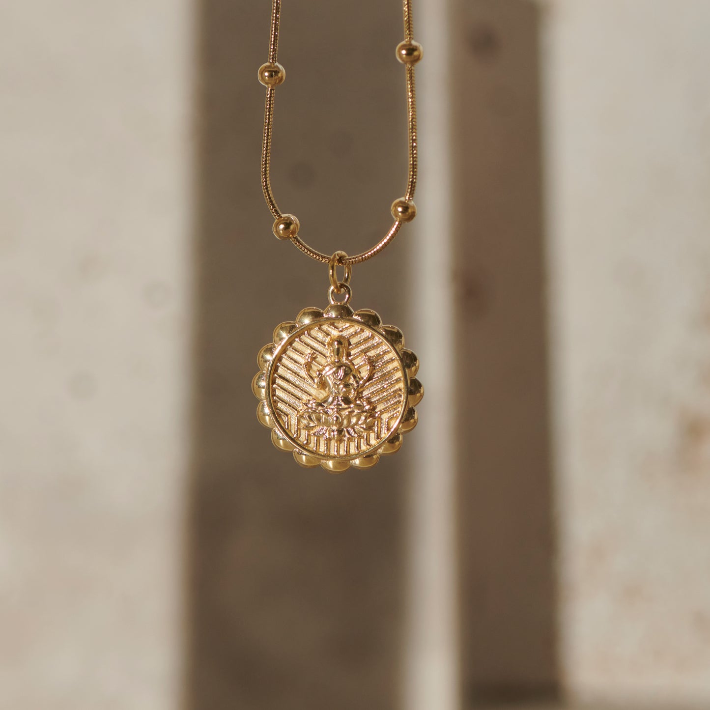 Gold lakshmi necklace with a round pendant on a neutral background