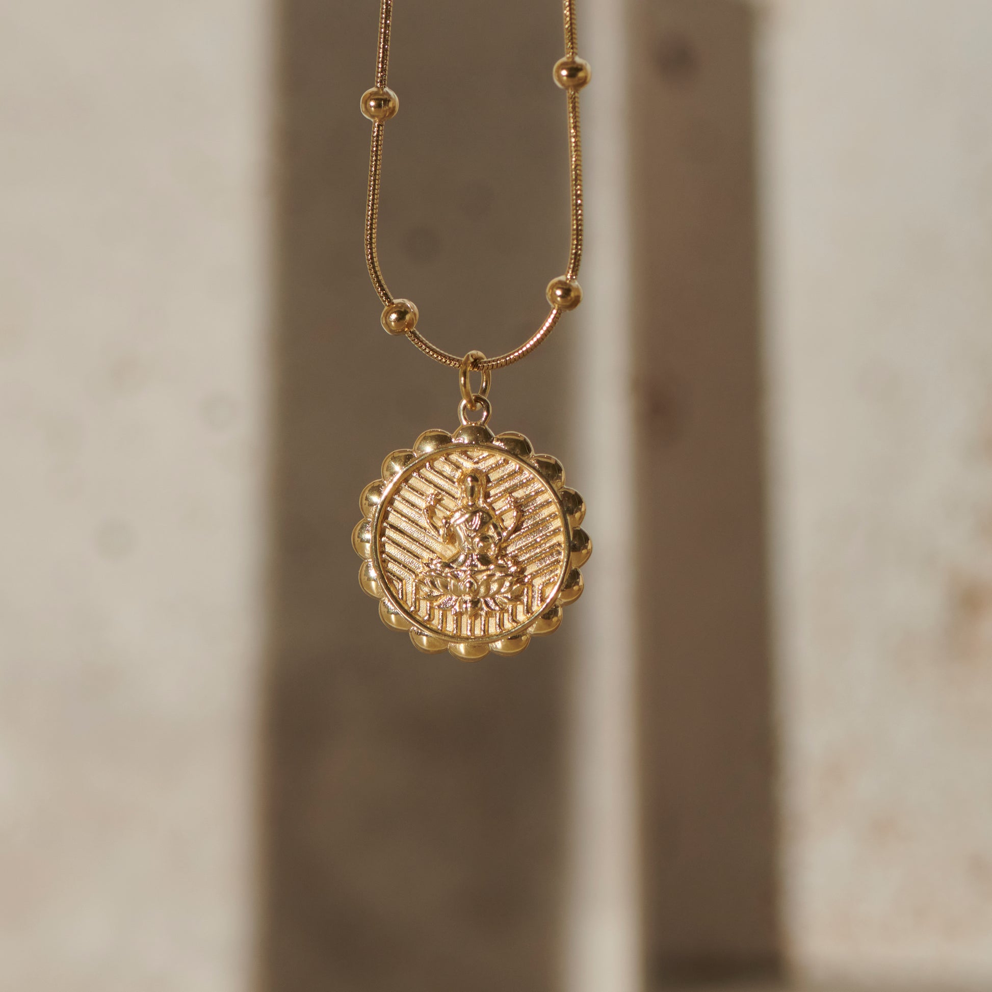 Gold lakshmi necklace with a round pendant on a neutral background