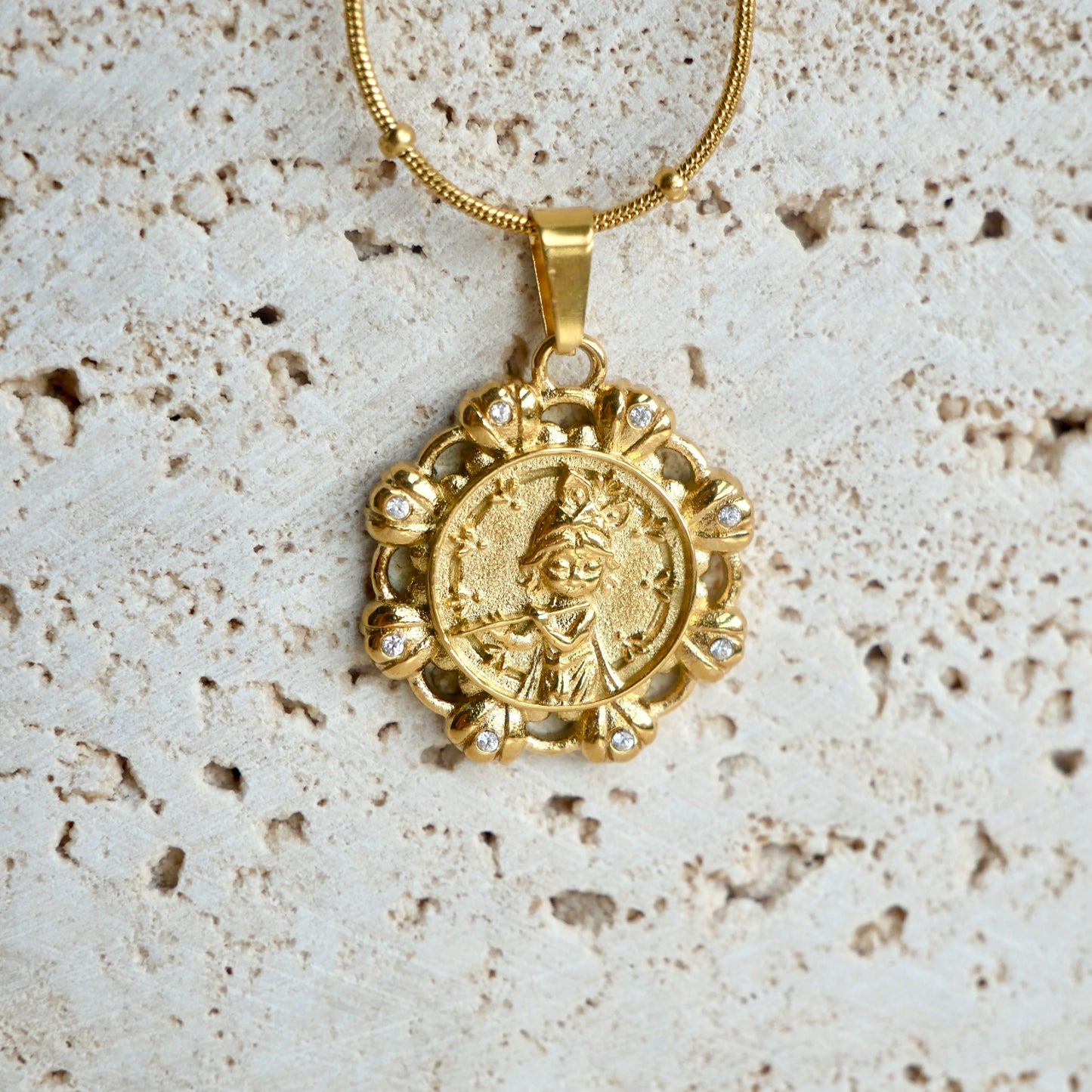 Gold krishna pendant necklace on a textured beige background