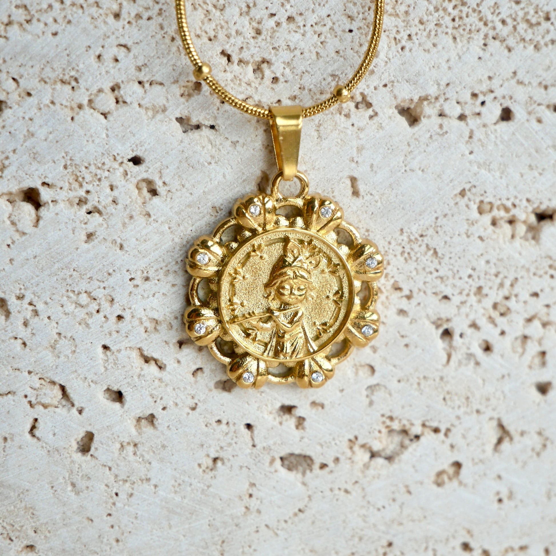 Gold krishna pendant necklace on a textured beige background