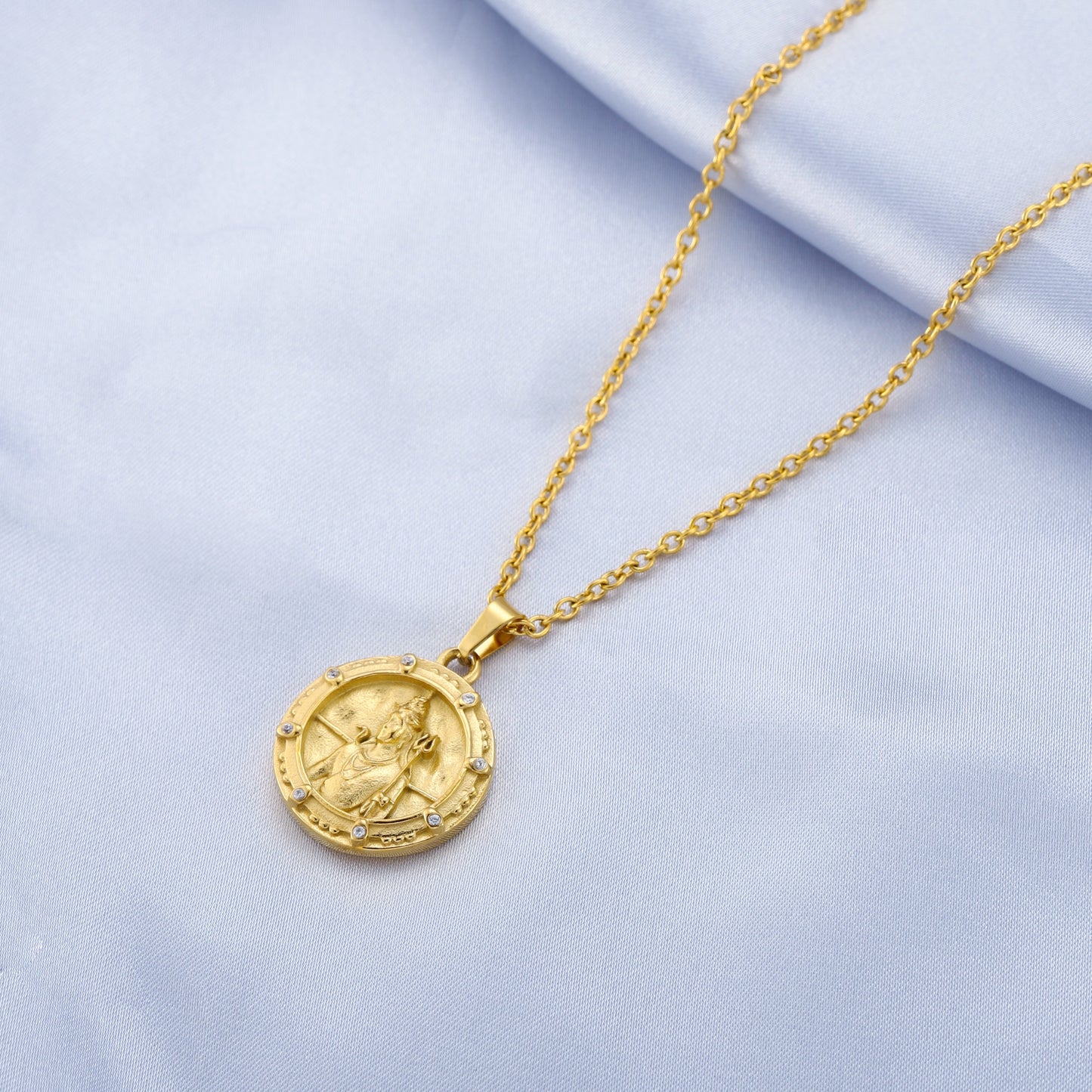 Gold shiva necklace with a round pendant on a light blue fabric background