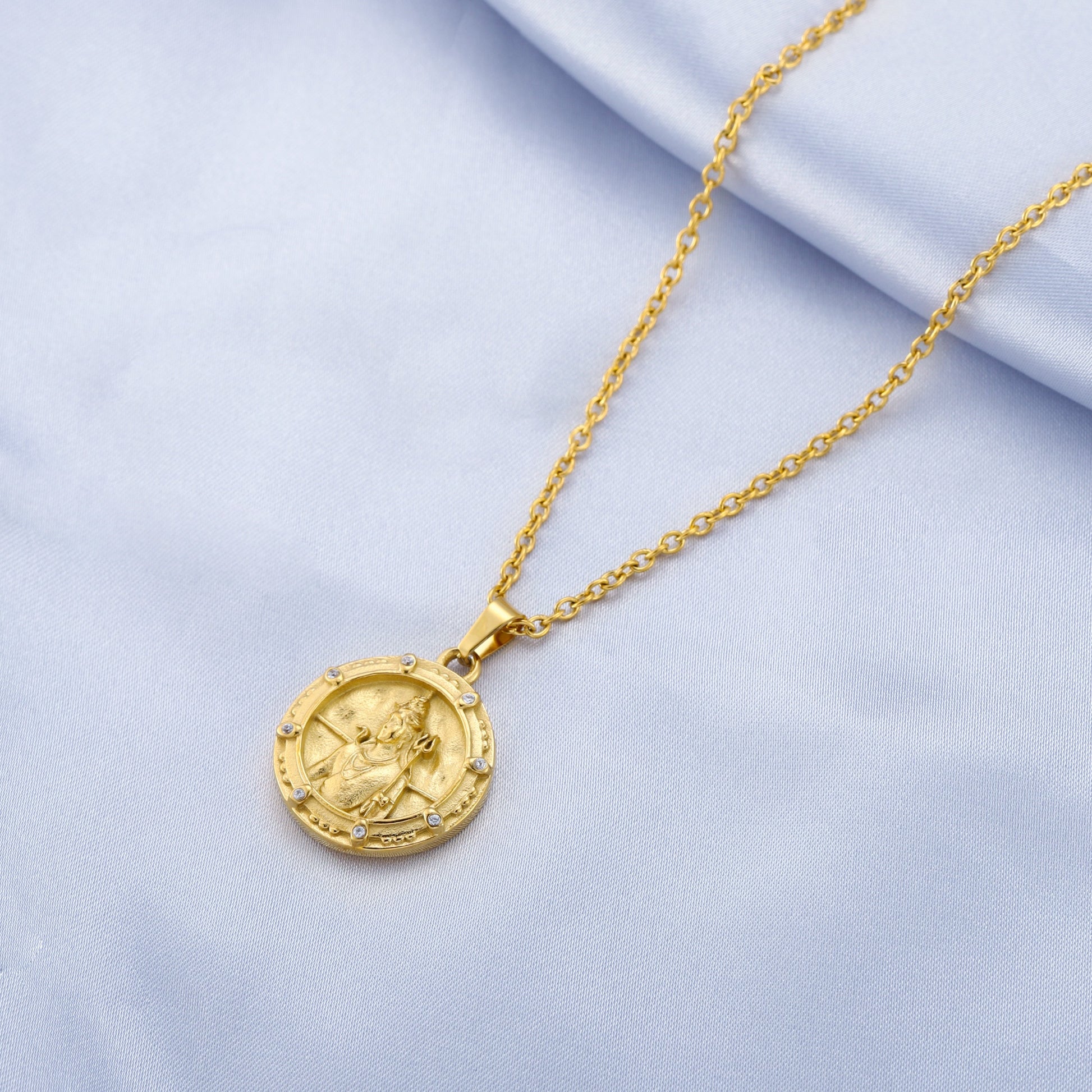 Gold shiva necklace with a round pendant on a light blue fabric background