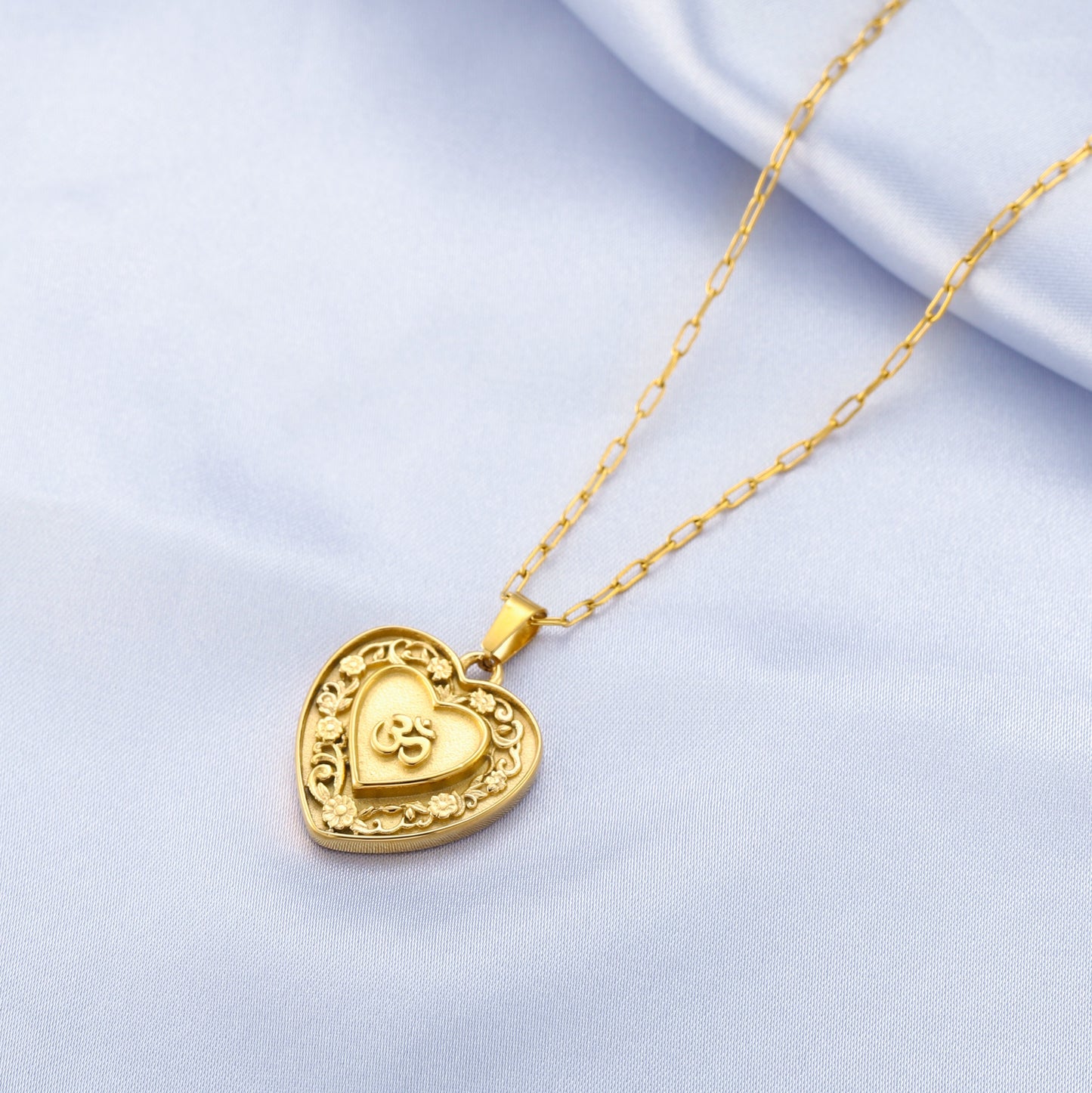 Gold heart-shaped om pendant necklace on a light blue background