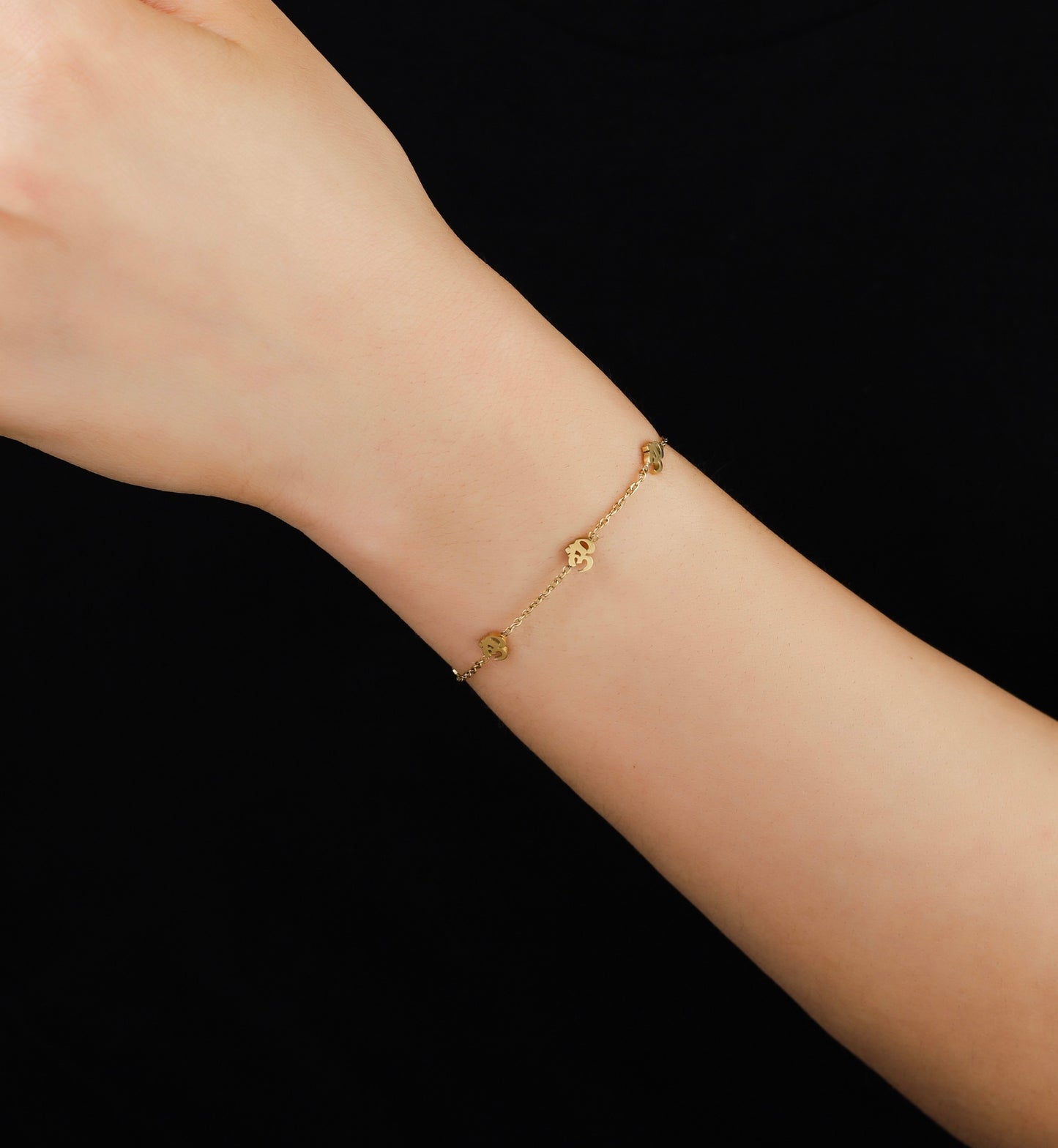 Gold bracelet on a person's wrist against a black background